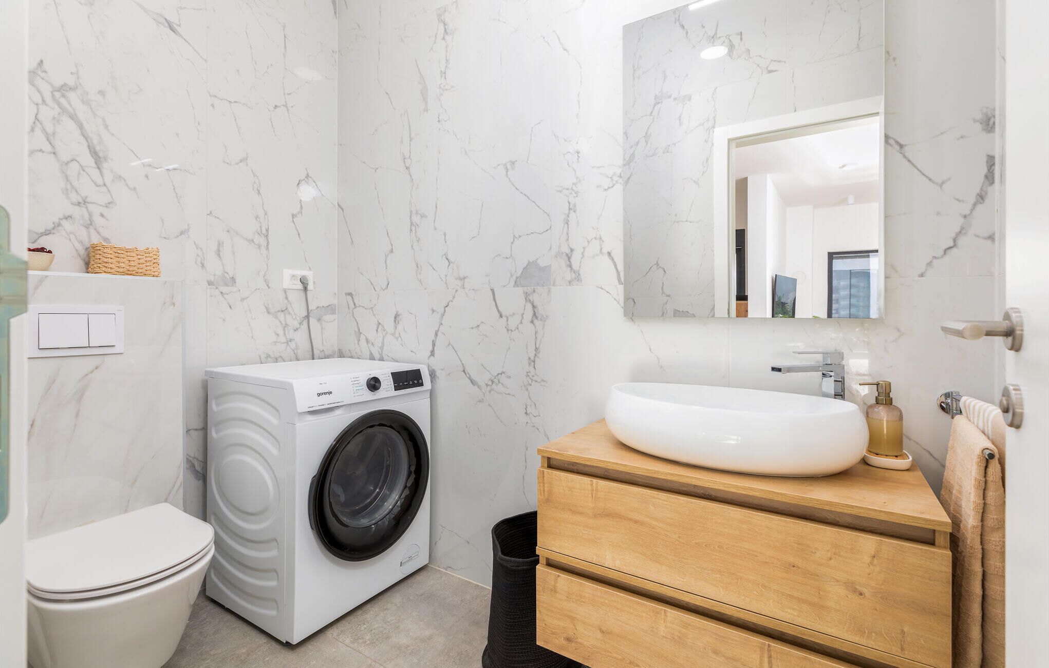 Un baño moderno con lavadora integrada, un lavabo con un espejo grande y un mueble de tocador de madera.