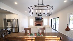 A spacious dining area with a wooden table and chairs, a brick fireplace, and a modern kitchen with stainless steel appliances. - The Campus Cottage on Elm is the ideal University of Oklahoma gameday residence (Norman)