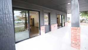 A covered outdoor area with glass doors leading to a building interior, brick pillars, and a concrete floor. - The Campus Cottage on Elm is the ideal University of Oklahoma gameday residence (Norman)