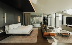 Una habitación de hotel moderna con una cama grande, un sofá, un televisor y vistas a la ciudad.