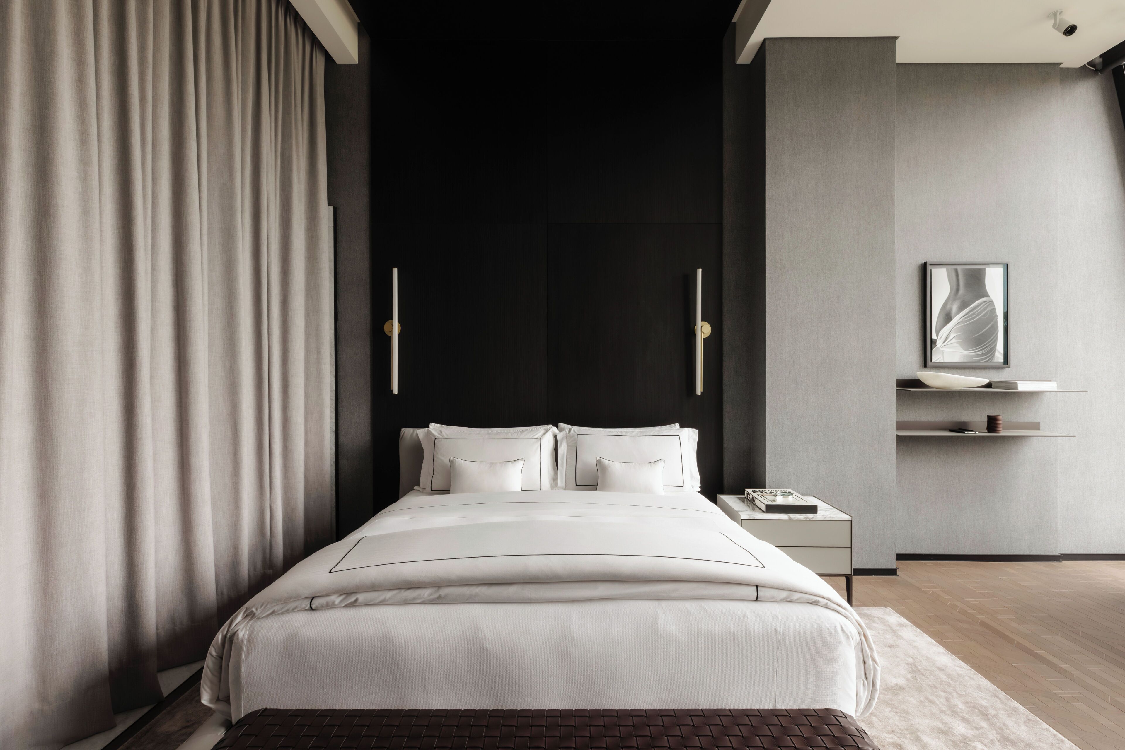 Un dormitorio moderno con una cama grande, una mesita de noche, un estante en la pared y una pared decorativa oscura.