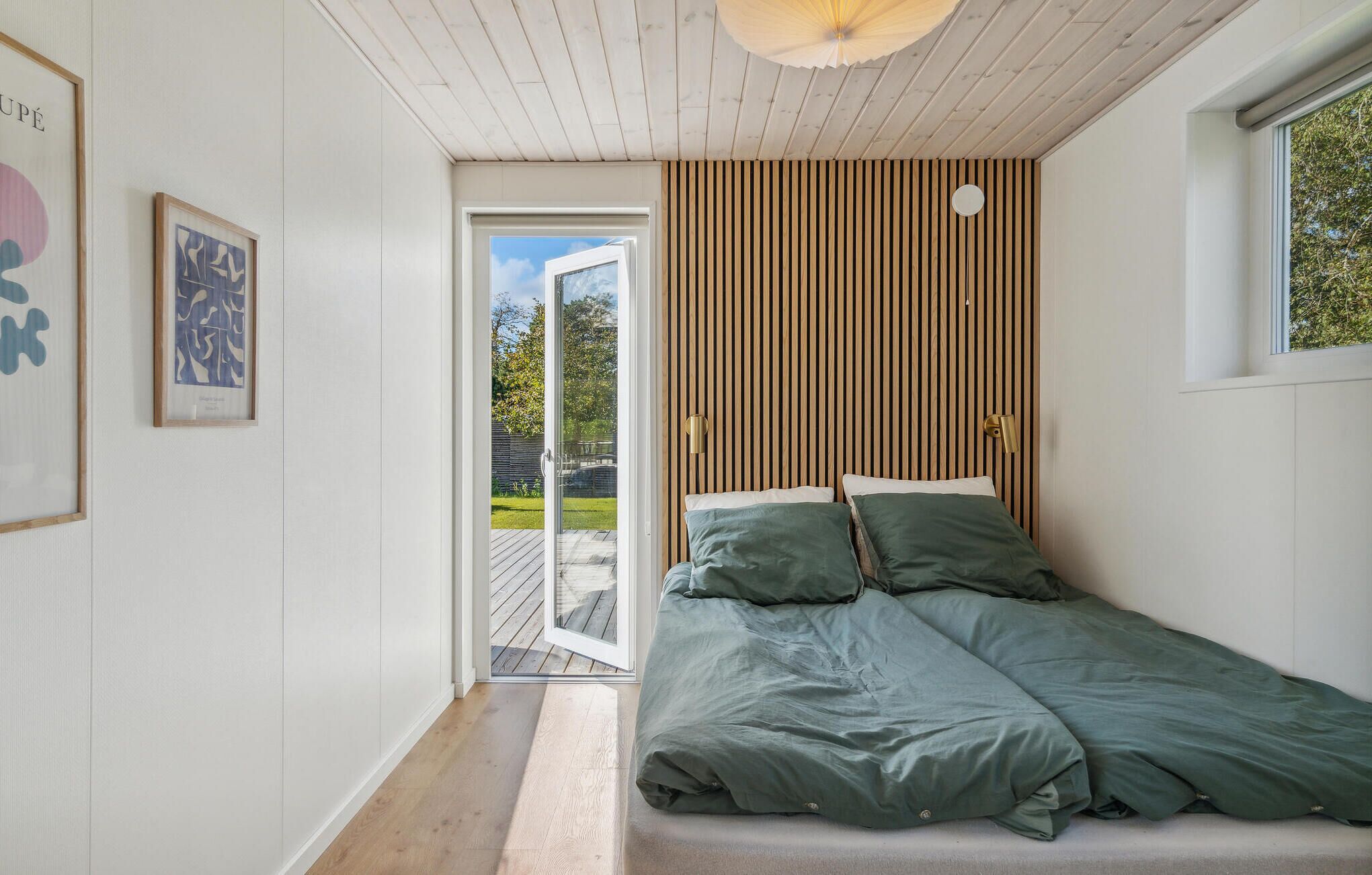Un dormitorio con cama, pared de listones de madera, ventana y puerta que da a un espacio exterior.