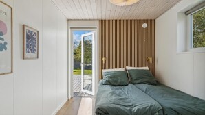 Makuuhuone, jossa on sänky, puusäleistä tehty seinä, ikkuna ja ovi, joka johtaa ulkotilaan.