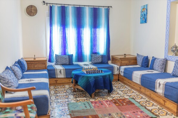 Ein Zimmer mit einer Sofagarnitur, einem Schachtisch und einem gemusterten Teppich.