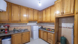 A kitchen with wooden cabinets, a sink, a refrigerator, and a gas cylinder.