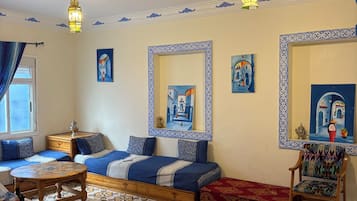 Una habitación con cama, una silla, una mesa y un tapete estampado.