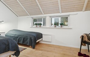 Un dormitorio con cama, ventana con plantas, radiador y suelo de madera.