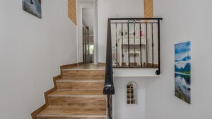 Un escalier avec des marches en bois et une rampe en métal noir, menant à une pièce où se trouve une commode blanche et un tableau représentant un paysage.