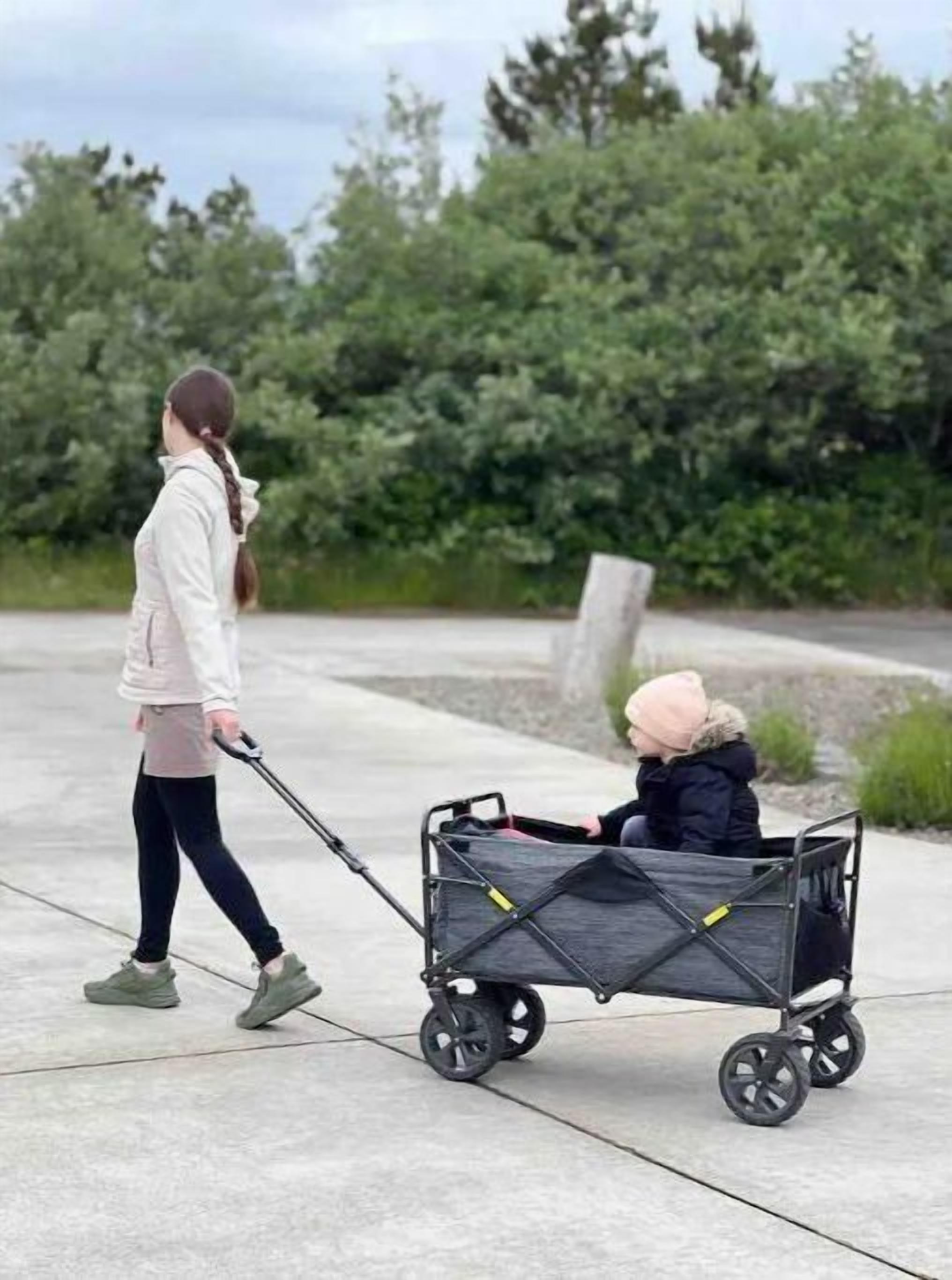 A woman walking a child in a stroller on a concrete path with greenery in the background.