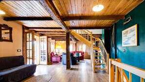 Un amplio salón con una escalera de madera, un sofá de cuero rojo y suelo de madera.