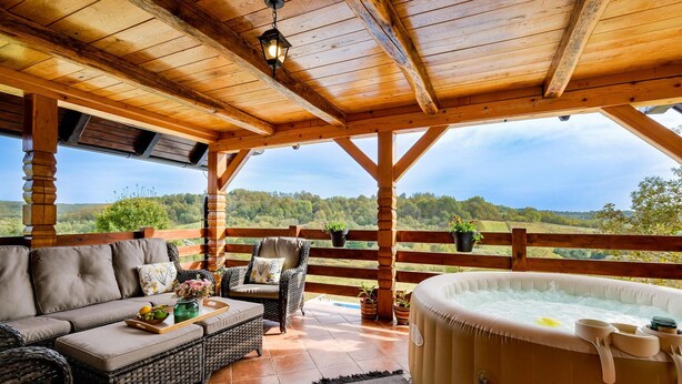 Una terraza de madera con un sofá, sillas, un jacuzzi y plantas en macetas.