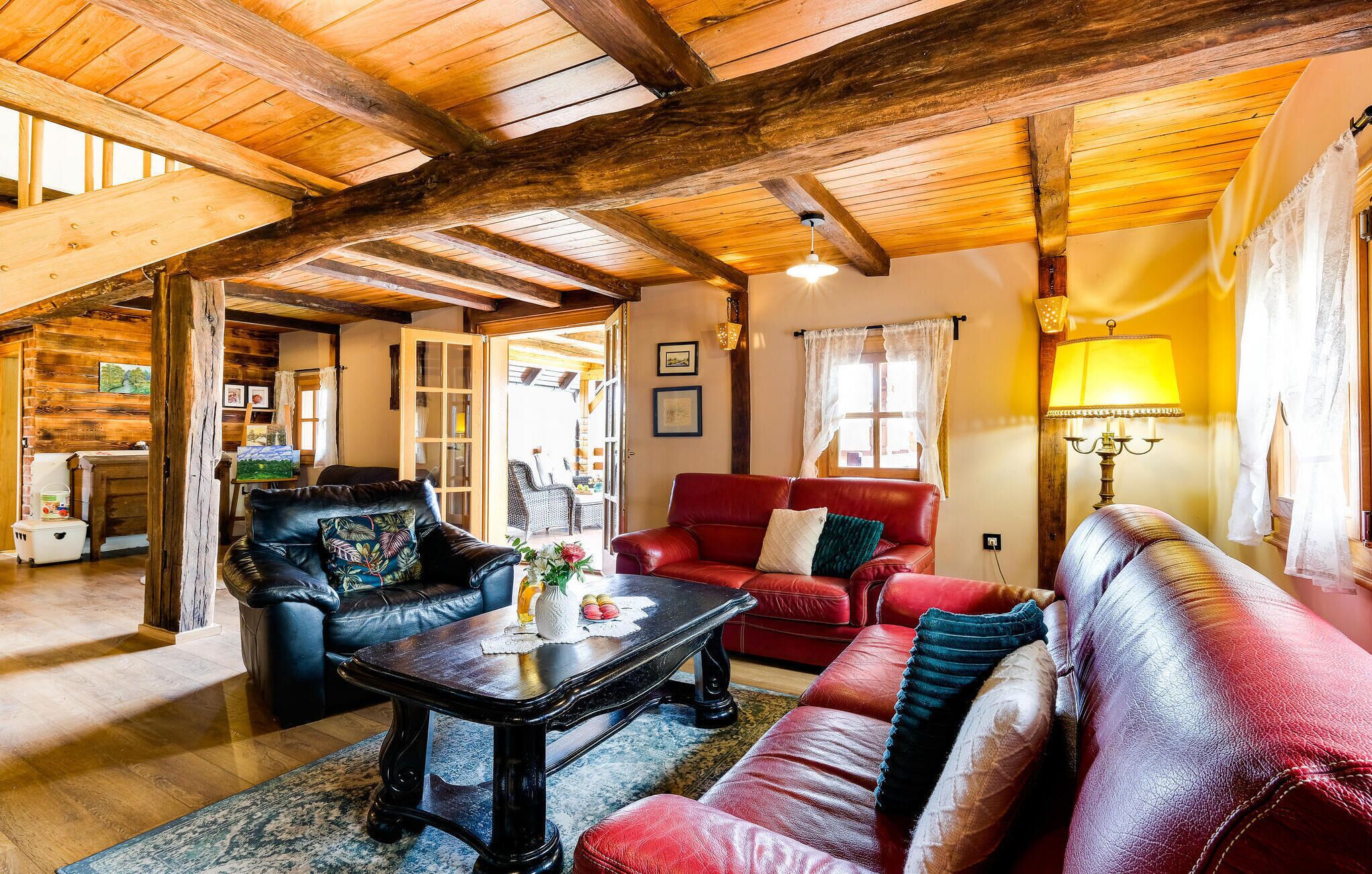 Un salon chaleureux avec un plafond en bois, un canapé en cuir rouge, un fauteuil en cuir noir et une table basse en bois.