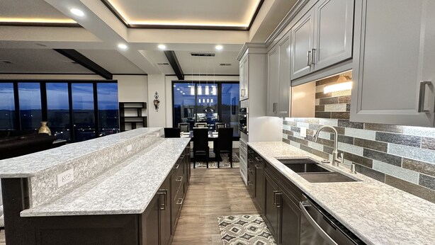 A modern kitchen with a central island, dark cabinetry, and a view of the city at dusk. - Encore Suite 1 @ The Skytower Penthouse  (Ashland)
