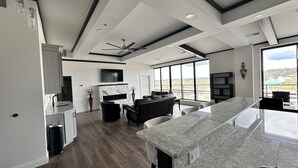 A modern kitchen with a marble countertop, a dining area with a large table, and a living space with a sofa and TV. - Encore Suite 1 @ The Skytower Penthouse  (Ashland)