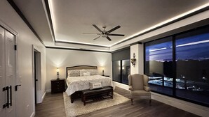 A modern bedroom with a large bed, a ceiling fan, and a view of the city at night. - Encore Suite 1 @ The Skytower Penthouse  (Ashland)