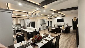 A modern kitchen with stainless steel appliances, a dining area with a table set for two, and a living area with a sofa and a TV. - Encore Suite 1 @ The Skytower Penthouse  (Ashland)