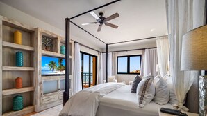 Een slaapkamer met een bed, een plafondventilator, uitzicht op de oceaan en een balkon.