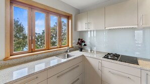 A modern kitchen with a large window, granite countertops, stainless steel appliances, and light-colored cabinetry. - Beachside Luxury - Laingholm Holiday Apartment (Auckland)