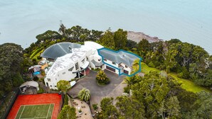An aerial view of a large, modern house with a spacious backyard, a tennis court, and a swimming pool. - Beachside Luxury - Laingholm Holiday Apartment (Auckland)