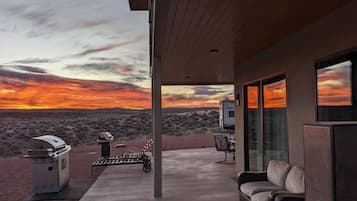 A modern outdoor patio with a view of a sunset over a desert landscape.
