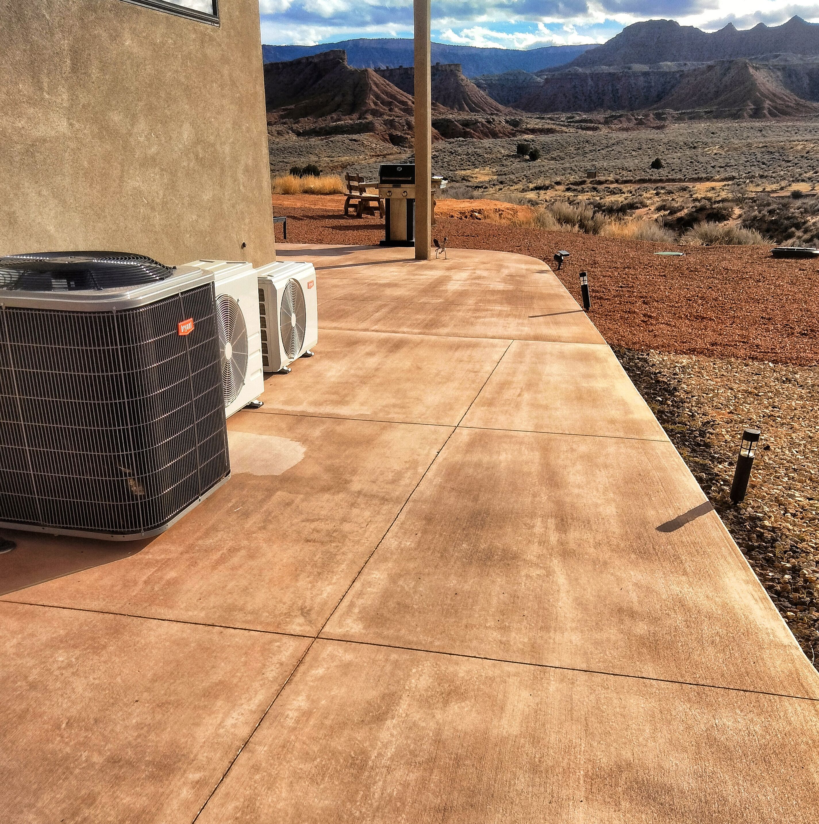 An outdoor patio with three air conditioning units, a concrete walkway, and a view of a mountainous landscape.