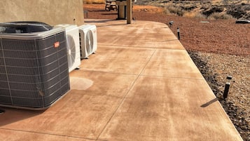 An outdoor patio with three air conditioning units, a concrete walkway, and a view of a mountainous landscape.