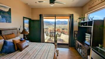 Un dormitorio con cama, ventilador de techo, televisión, escritorio y vista al desierto a través de una puerta corrediza.