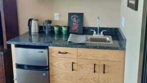 Una cocina funcional con armarios de madera, un refrigerador de acero inoxidable, un lavamanos y una encimera con una tetera y tazas.