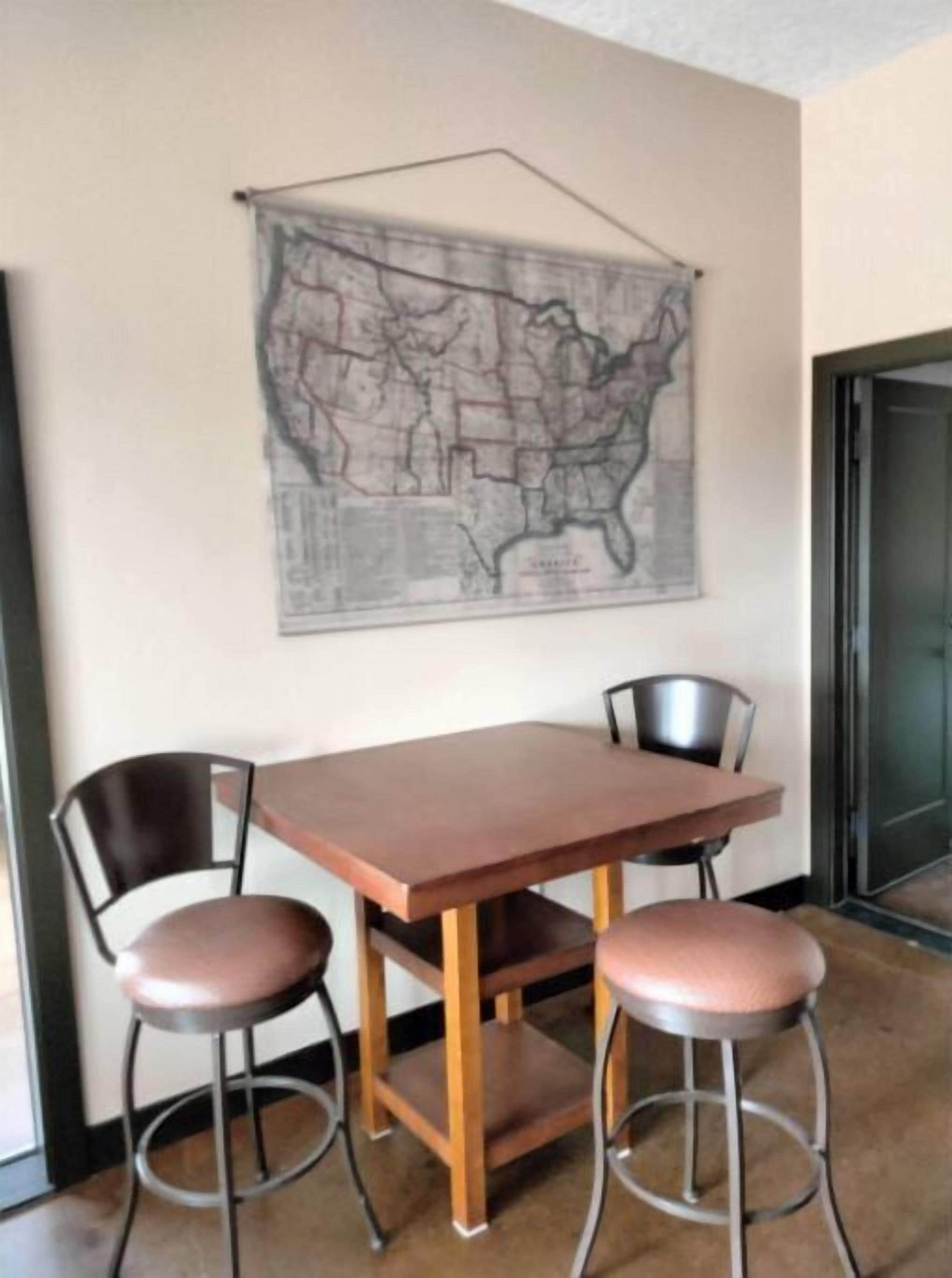 Un comedor con una mesa de madera y dos taburetes tipo barra, un mapa en la pared y una puerta a la derecha.