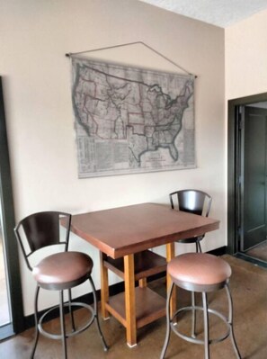 Un comedor con una mesa de madera y dos taburetes tipo barra, un mapa en la pared y una puerta a la derecha.