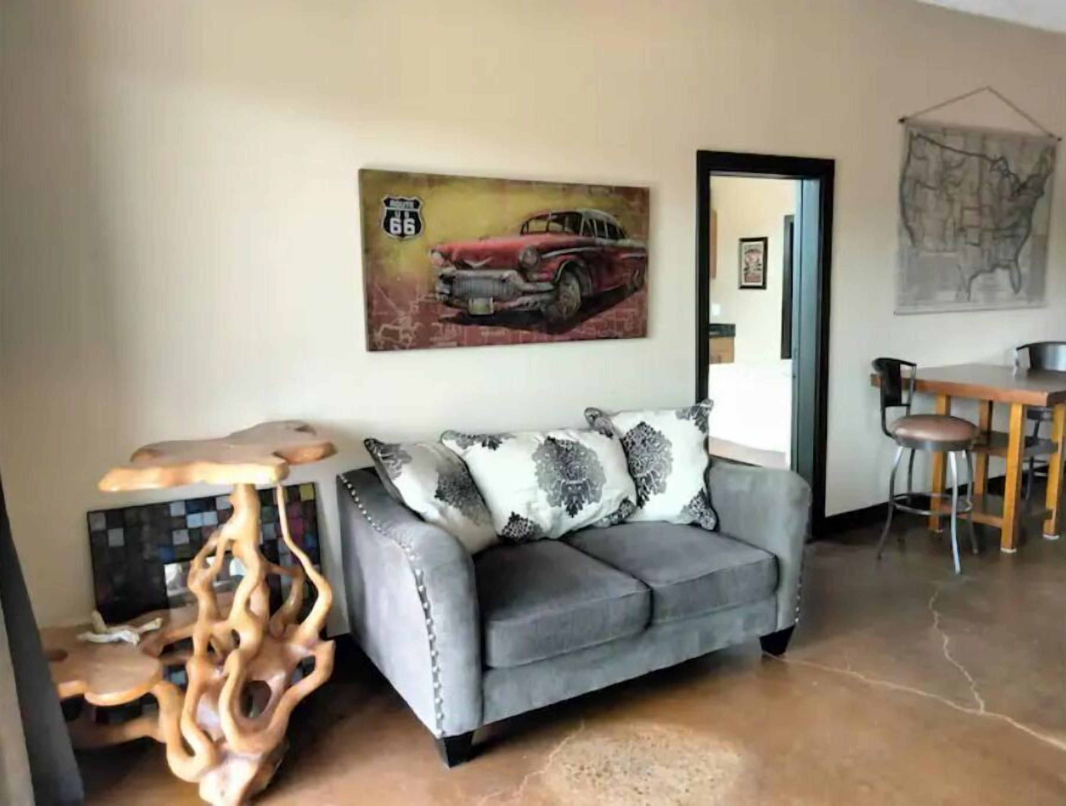 Una sala de estar con un sofá gris, una mesa de centro de madera y un cuadro de un coche antiguo.