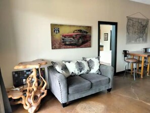 Una sala de estar con un sofá gris, una mesa de centro de madera y un cuadro de un coche antiguo.