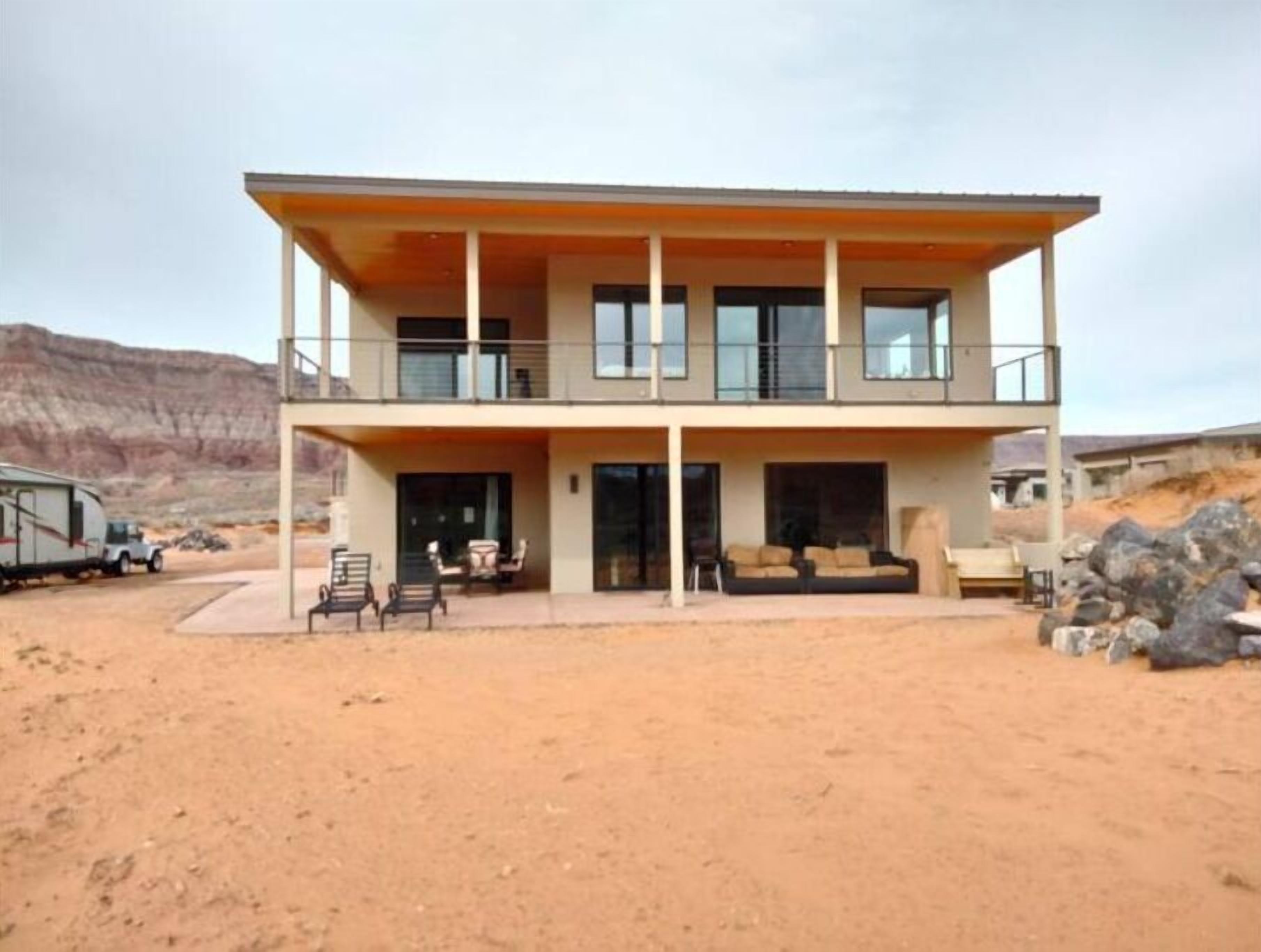 Un edificio de dos pisos con un balcón, un patio cubierto y un paisaje desértico al fondo.