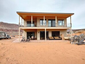 Un edificio de dos pisos con un balcón, un patio cubierto y un paisaje desértico al fondo.