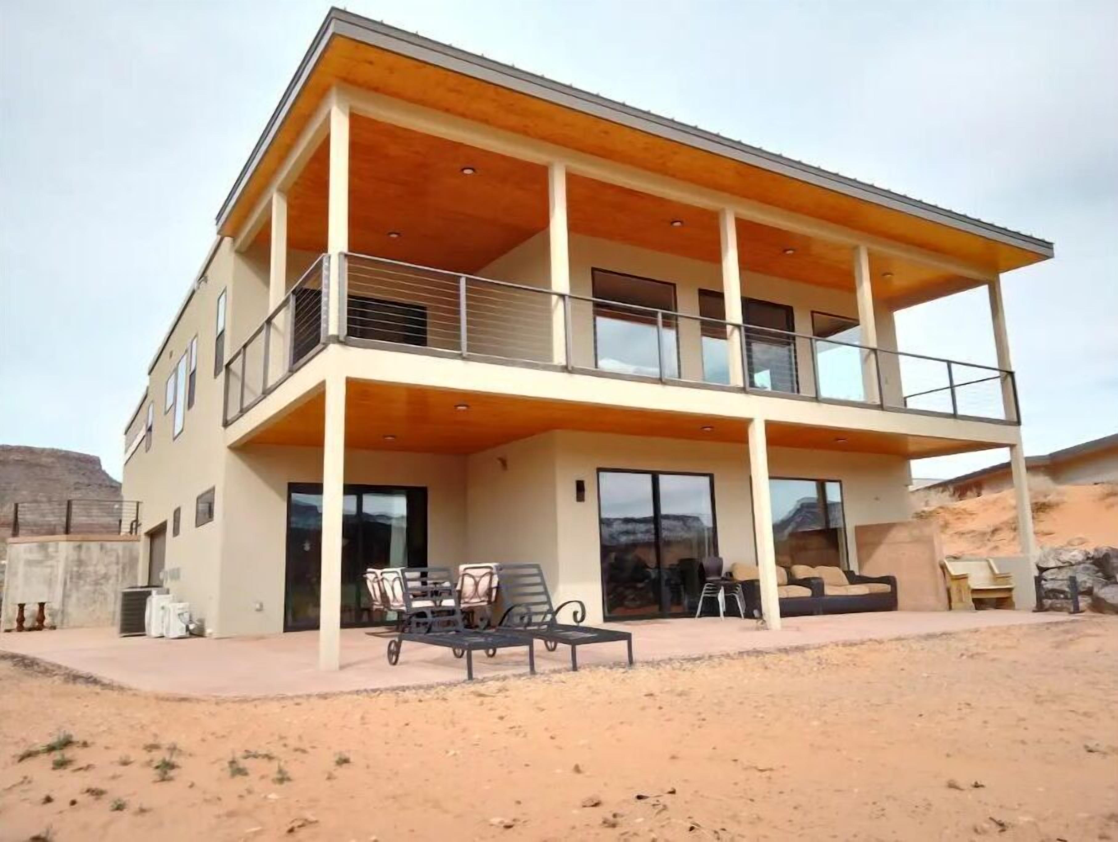 Una casa moderna de dos pisos con un patio cubierto, ventanas grandes y techo plano.