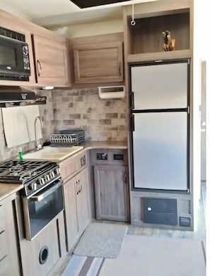 A compact kitchen with a gas stove, microwave, and a refrigerator.