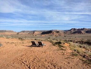 A desert landscape with a pair of empty lounge chairs facing a range of hills.