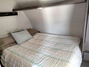 A bedroom with a bed, pillows, and a window with blinds.