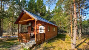 A wooden cabin with a porch, a small dining area, and a window overlooking the forest.