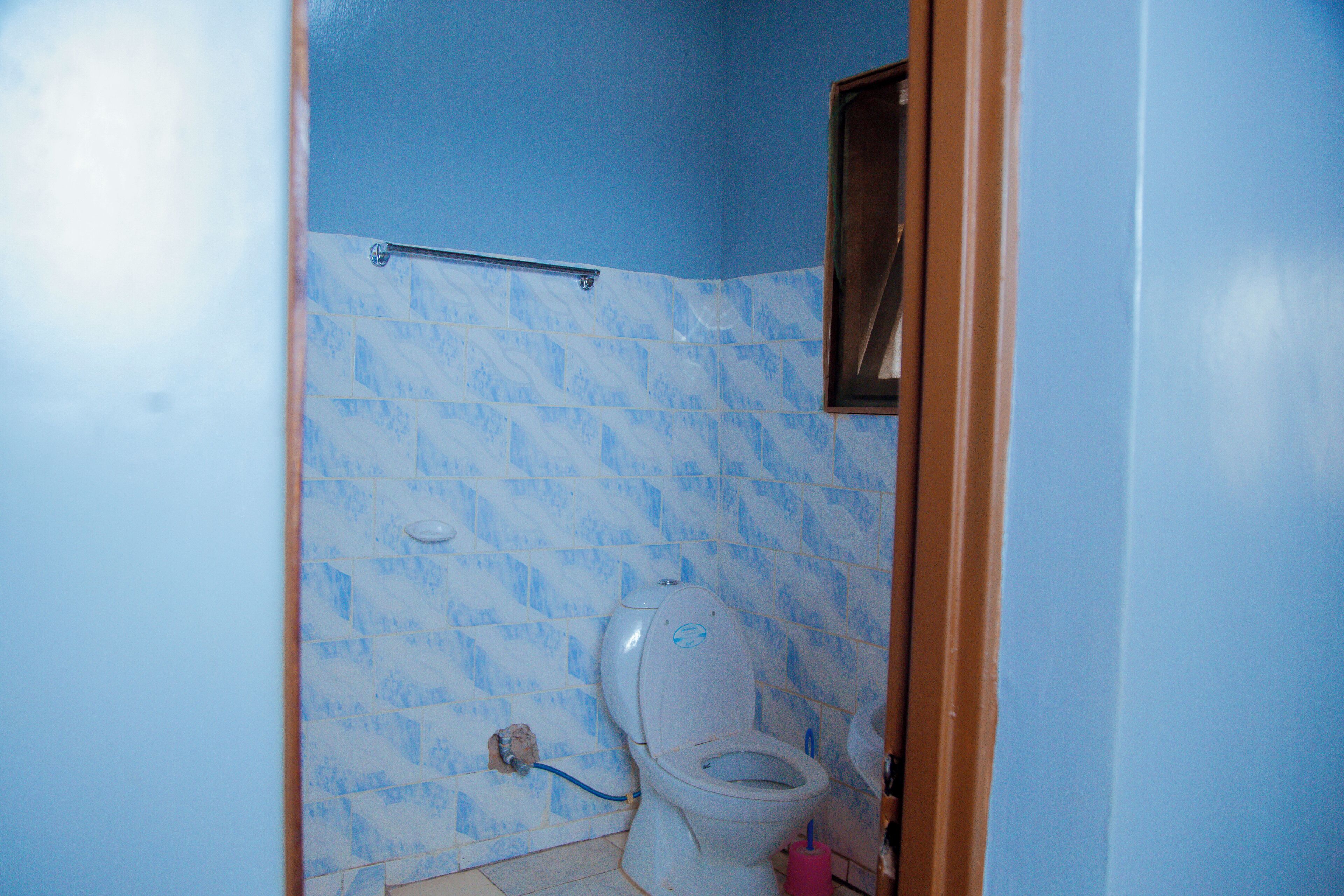 A bathroom with a toilet, a handrail, and a tiled wall.