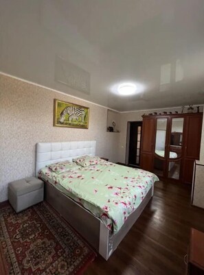 Een slaapkamer met een bed, een klein nachtkastje, een vloerkleed, een kledingkast en een spiegel.