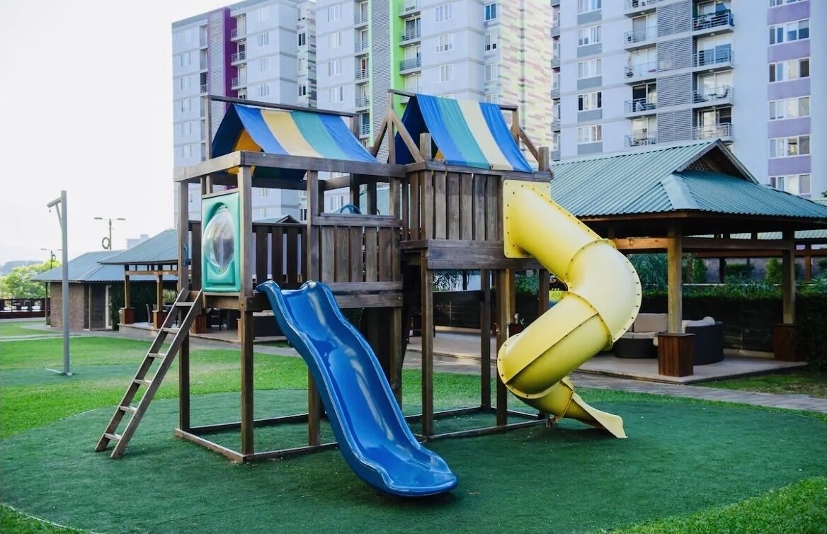 A playground with a blue slide and a yellow slide, surrounded by a wooden play structure.