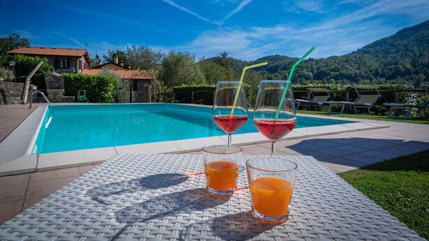 Zona junto a la piscina con dos vasos de bebida roja y dos vasos de jugo de naranja sobre una mesa de mimbre.
