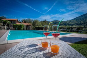 Relax by the pool surrounded by lush greenery and a stone building.