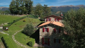 Una casa de piedra con contraventanas rojas, rodeada por un jardín cuidado y un telón de fondo montañoso pintoresco.