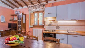 A kitchen with wooden cabinets, a gas stove, and a dining table with a bowl of vegetables. - Apartment in Abetone with 3 bedrooms sleeps 6 (Cutigliano)