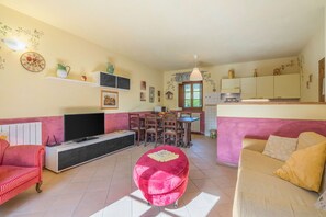 Una sala de estar con televisor, un pouf rosa, un sofá a rayas rojas y un sofá beige.