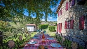 An outdoor dining area with a checkered tablecloth, metal chairs, and a stone building with red shutters in the background. - Apartment in Abetone with 2 bedrooms sleeps 4 (Abetone)