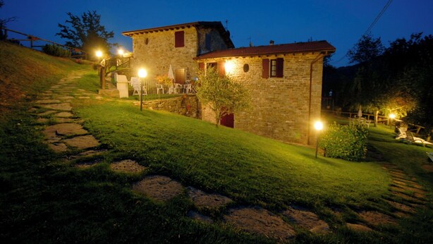 A stone house with a red roof, a stone staircase, and a well-lit garden at dusk. - Apartment in Abetone with 2 bedrooms sleeps 4 (Abetone)
