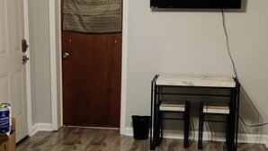 Una sala de estar con ventilador de techo, un televisor de pantalla plana montado en la pared, una puerta de madera y un banco con tapa de mármol blanco.